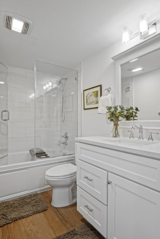 bathroom featuring visible vents, combined bath / shower with glass door, toilet, wood finished floors, and vanity