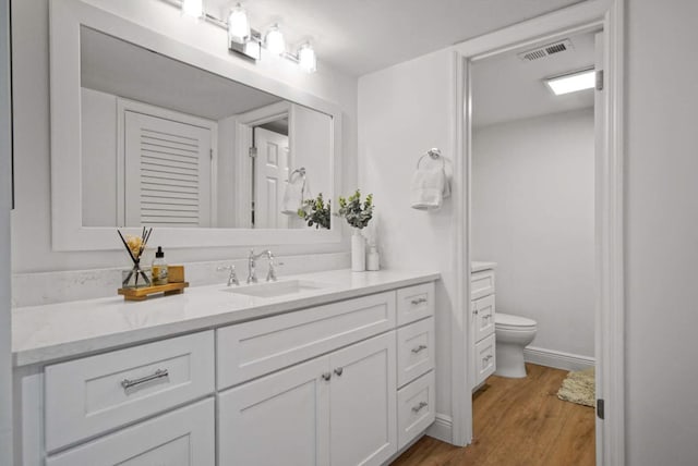 bathroom featuring toilet, vanity, wood finished floors, baseboards, and visible vents