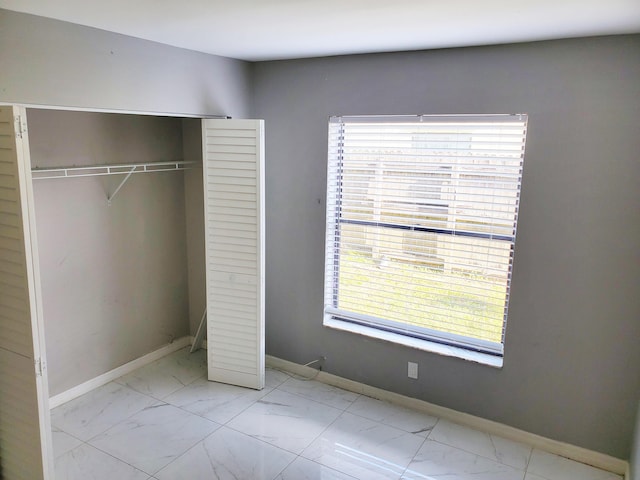 unfurnished bedroom featuring baseboards, marble finish floor, and a closet