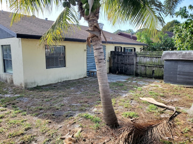 back of property with stucco siding, an outdoor structure, fence, a storage shed, and a shingled roof