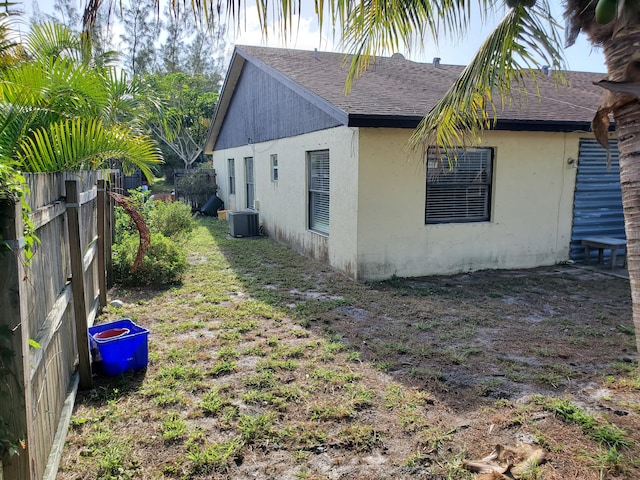 view of side of home with stucco siding, a shingled roof, fence, and cooling unit