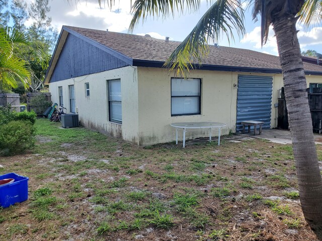 back of property with central air condition unit, a shingled roof, stucco siding, and fence