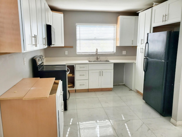 kitchen featuring freestanding refrigerator, stainless steel range with electric stovetop, a sink, and white cabinets