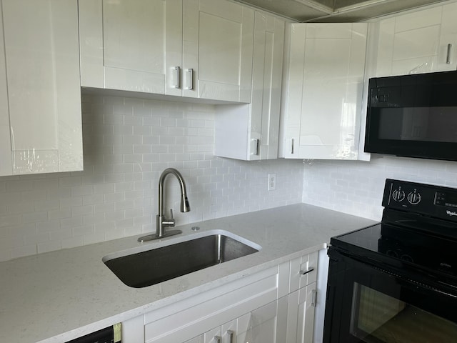 kitchen with black appliances, a sink, light stone counters, backsplash, and white cabinetry