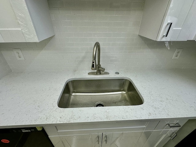 interior details with backsplash, white cabinets, light stone countertops, and a sink