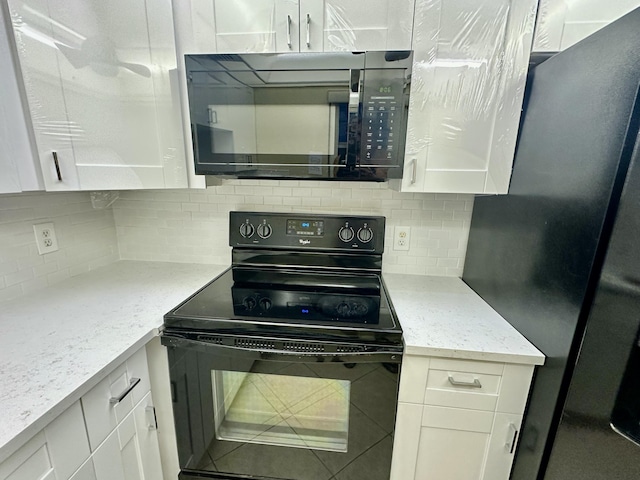 kitchen featuring light stone countertops, decorative backsplash, freestanding refrigerator, black electric range oven, and white cabinetry
