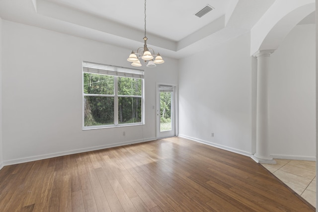 unfurnished room featuring visible vents, a tray ceiling, arched walkways, decorative columns, and a notable chandelier