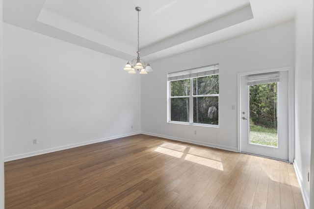 empty room with baseboards, a raised ceiling, an inviting chandelier, and wood finished floors