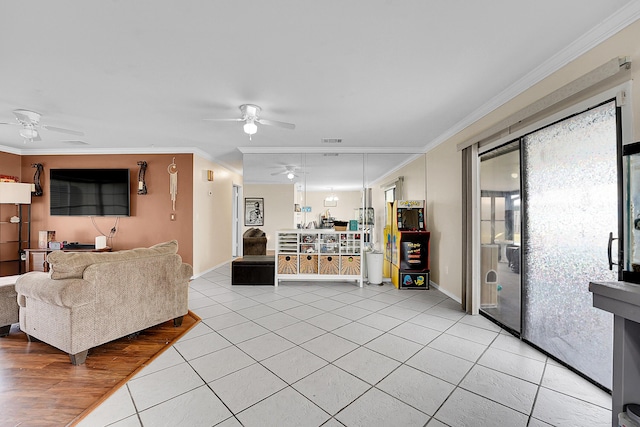 living room featuring a ceiling fan, light tile patterned floors, crown molding, and visible vents
