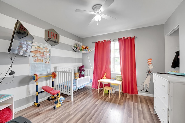 bedroom featuring baseboards, wood finished floors, ceiling fan, and a nursery area