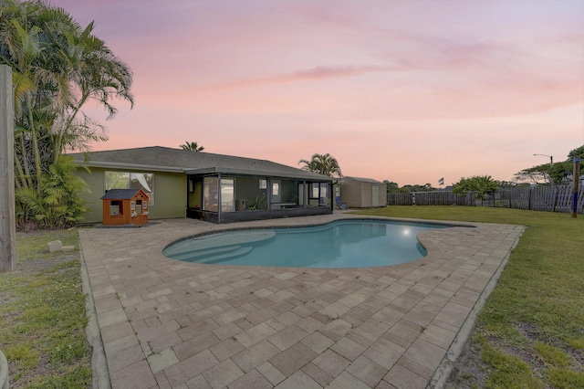 pool at dusk featuring a patio, a fenced backyard, a storage unit, a lawn, and an outdoor structure