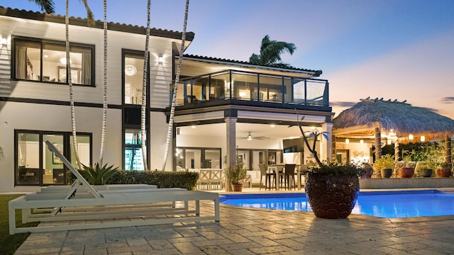 1526 SE 11th St, Deerfield Beach, FL 33441 - back of property at dusk featuring a patio area, a balcony, a ceiling fan, an outdoor pool, and stucco siding
