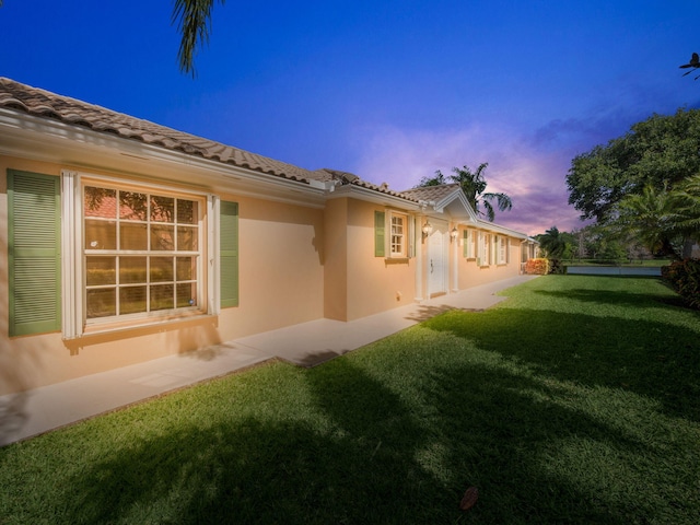 back of house featuring a lawn, a tile roof, and stucco siding