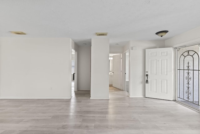entrance foyer with a textured ceiling, light wood finished floors, and visible vents