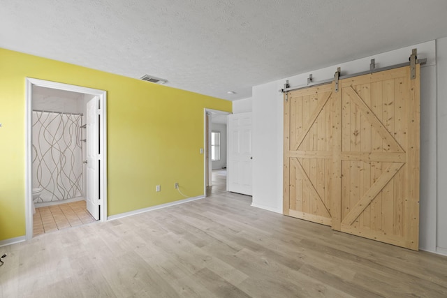 unfurnished bedroom featuring light wood-type flooring, visible vents, ensuite bathroom, and a textured ceiling