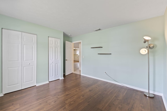 unfurnished bedroom featuring dark wood-style floors, visible vents, two closets, and baseboards