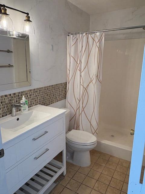 full bath with a stall shower, toilet, vanity, decorative backsplash, and tile walls