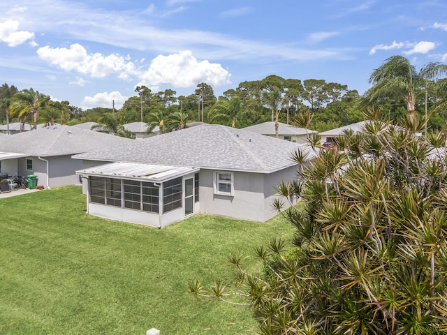 back of property with roof with shingles, a sunroom, stucco siding, and a yard