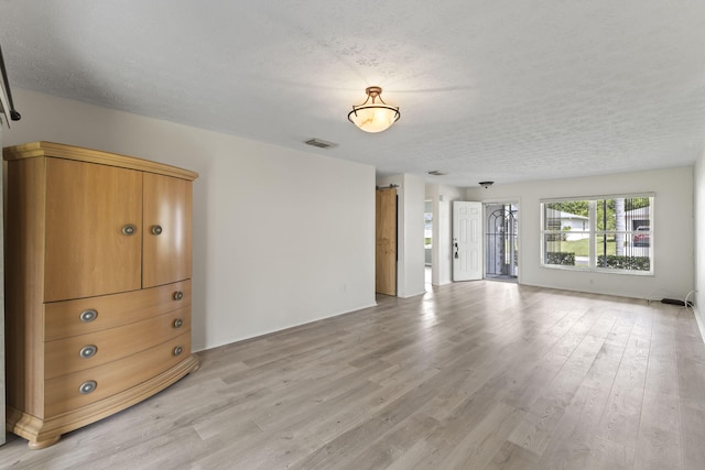 interior space featuring a textured ceiling, light wood finished floors, and visible vents