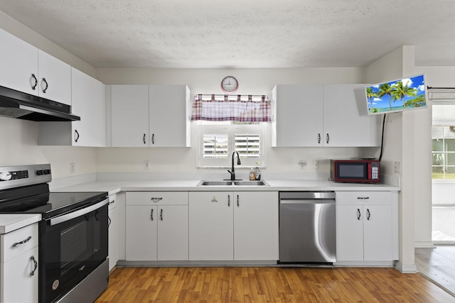 kitchen with light countertops, stainless steel appliances, under cabinet range hood, a sink, and light wood finished floors