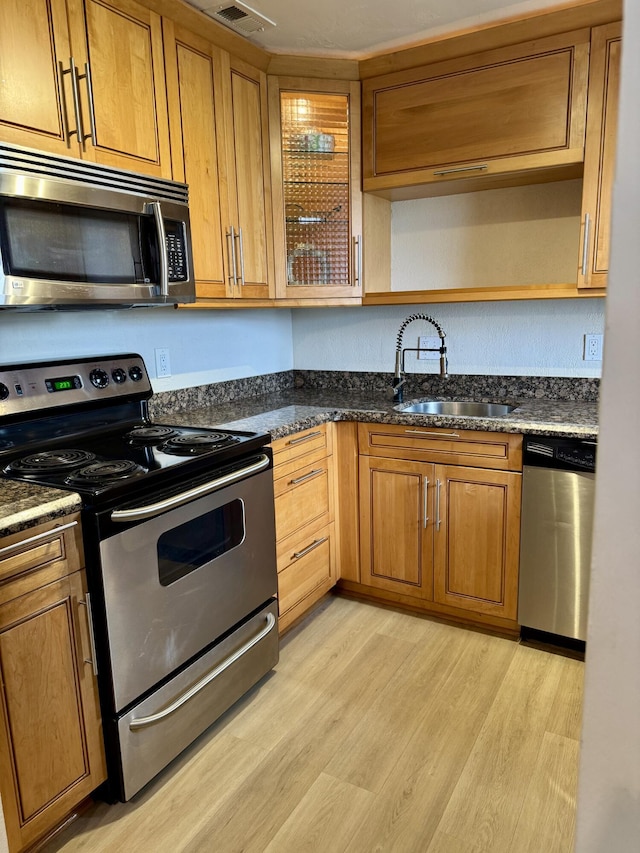 kitchen with brown cabinets, appliances with stainless steel finishes, a sink, open shelves, and light wood-type flooring