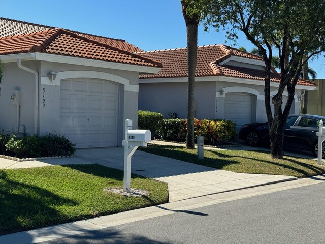 mediterranean / spanish home with stucco siding, driveway, a front yard, a garage, and a tiled roof
