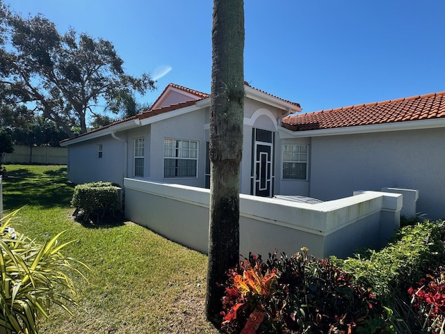 view of home's exterior featuring stucco siding, fence, a lawn, and a tiled roof