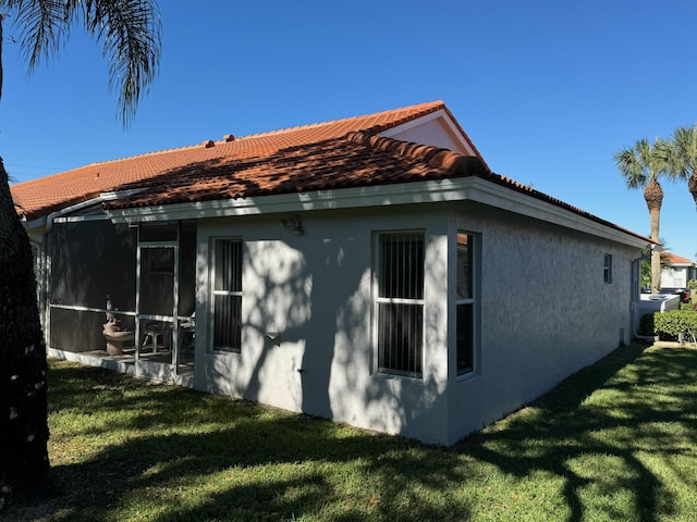 view of side of home featuring stucco siding, a sunroom, a yard, and a tiled roof