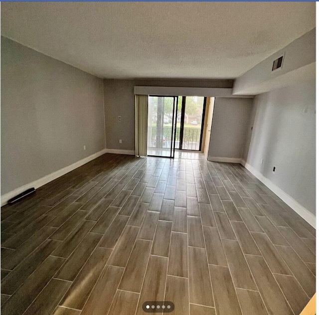 empty room featuring a textured ceiling, visible vents, baseboards, and dark wood-style flooring
