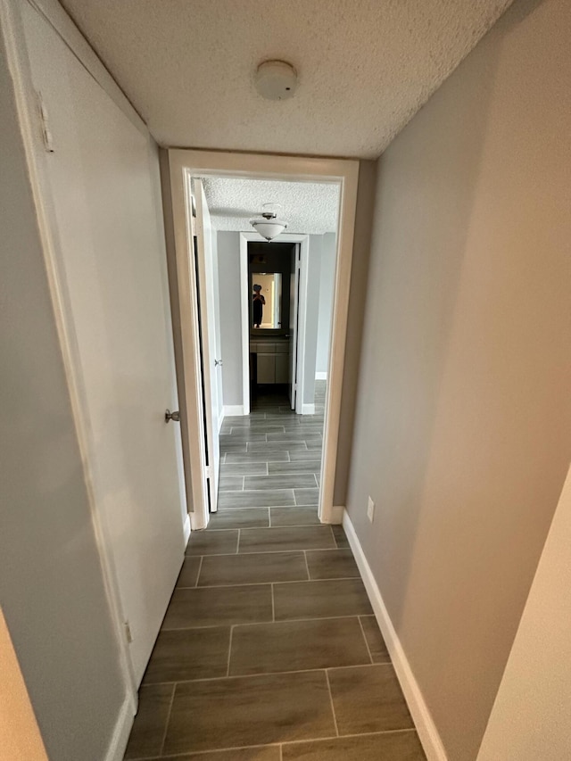 hall featuring wood finish floors, baseboards, and a textured ceiling