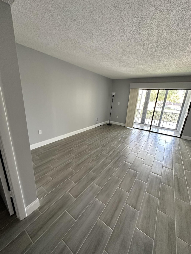 empty room with a textured ceiling, wood finish floors, and baseboards