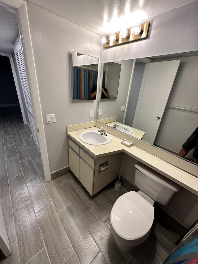 bathroom featuring baseboards, toilet, vanity, and wood tiled floor