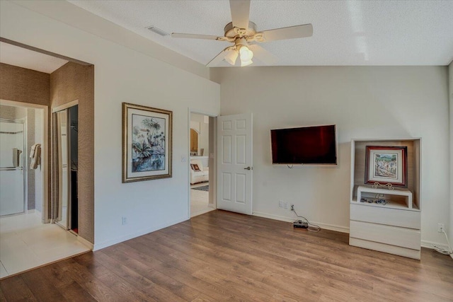 unfurnished living room with a ceiling fan, wood finished floors, a textured ceiling, lofted ceiling, and baseboards