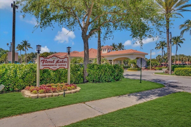 community sign with curved driveway and a lawn