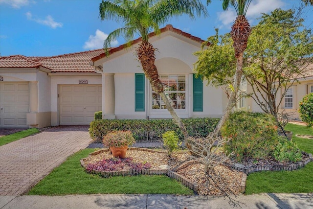 mediterranean / spanish house with stucco siding, a tile roof, a garage, and decorative driveway