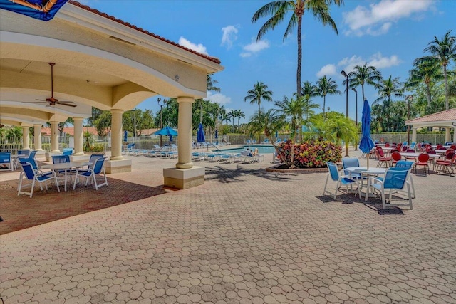 view of patio with a community pool, fence, and ceiling fan