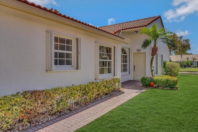 property entrance with a tile roof, stucco siding, and a yard