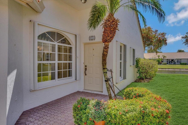 entrance to property featuring stucco siding and a lawn