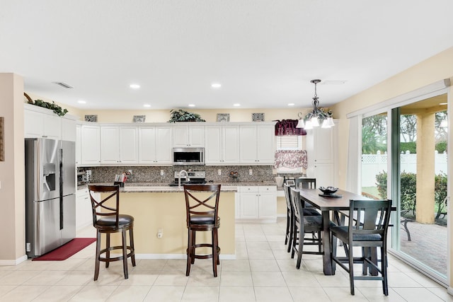 kitchen with decorative backsplash, white cabinets, visible vents, stainless steel appliances, and a center island