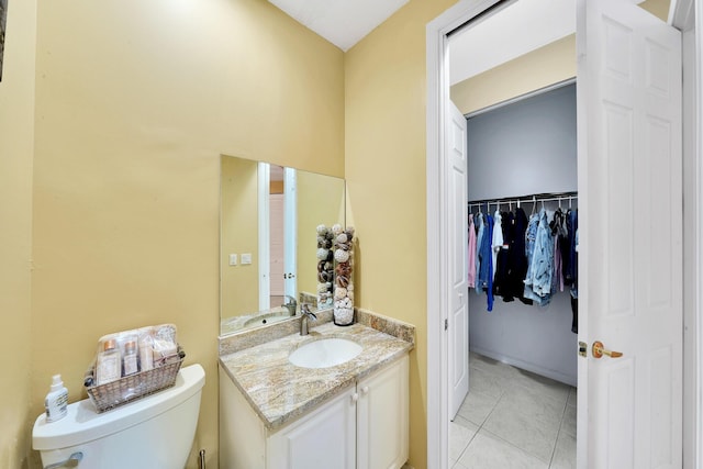 bathroom featuring toilet, vanity, tile patterned flooring, and a walk in closet