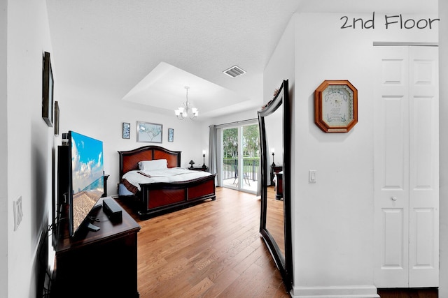 bedroom with wood finished floors, access to exterior, visible vents, a notable chandelier, and a tray ceiling