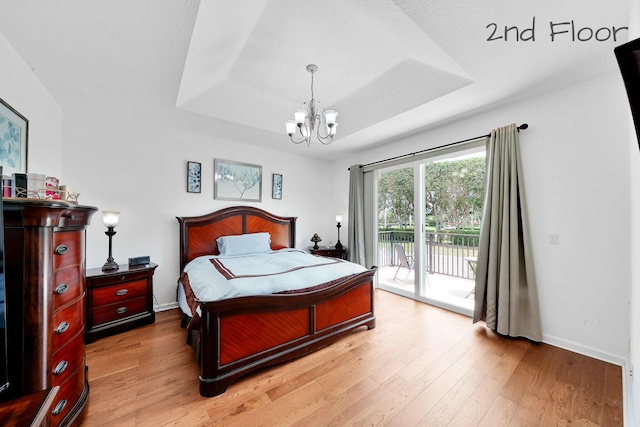 bedroom featuring light wood finished floors, a chandelier, access to outside, a raised ceiling, and baseboards