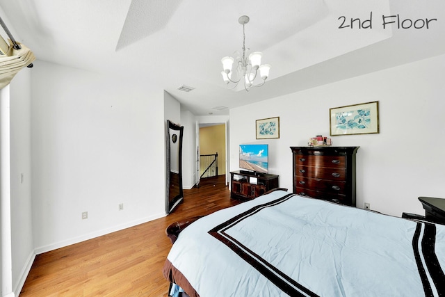 bedroom featuring visible vents, an inviting chandelier, wood finished floors, and baseboards