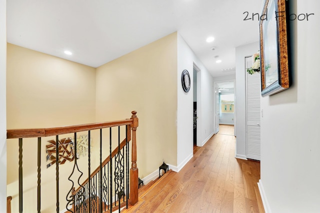 hallway with light wood-style floors, baseboards, an upstairs landing, and recessed lighting