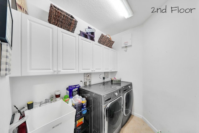 laundry area featuring a sink, cabinet space, washer and clothes dryer, light tile patterned floors, and baseboards