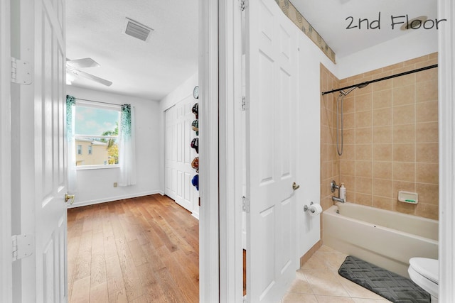 bathroom featuring hardwood / wood-style floors, toilet, baseboards, visible vents, and washtub / shower combination