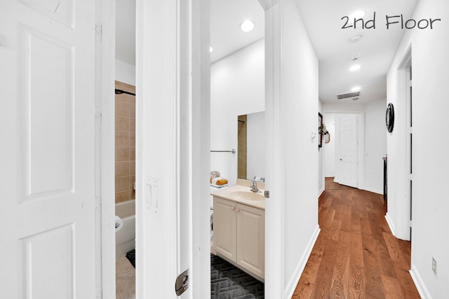 hall with recessed lighting, a sink, visible vents, baseboards, and wood finished floors