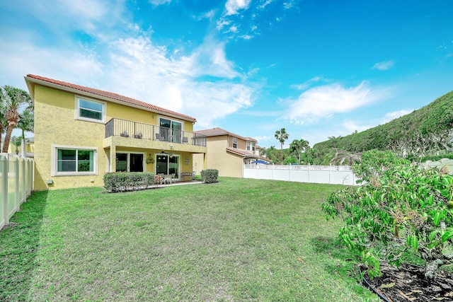 rear view of house featuring a fenced backyard, stucco siding, a patio area, a balcony, and a lawn