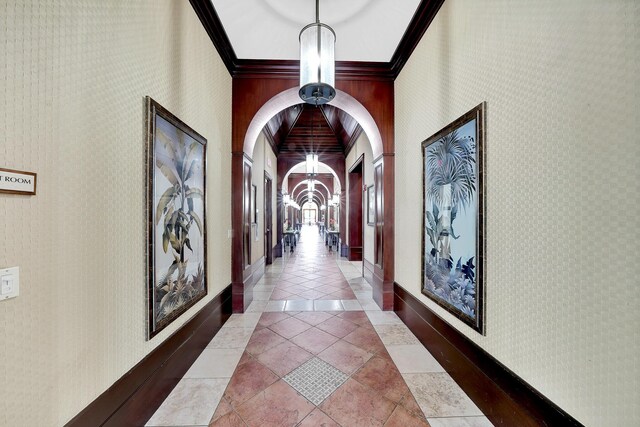 hallway featuring a notable chandelier, tile patterned floors, baseboards, ornamental molding, and wallpapered walls
