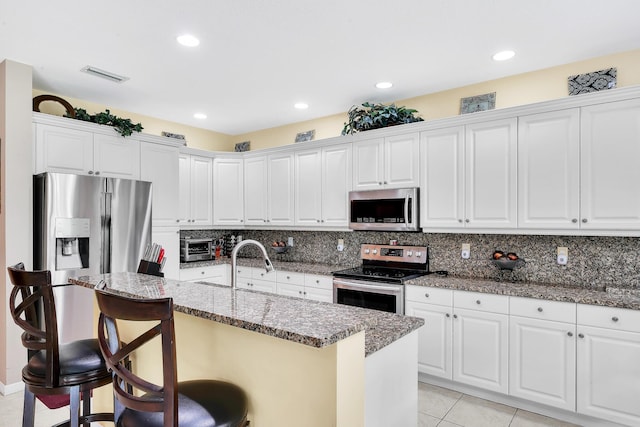 kitchen with visible vents, stainless steel appliances, white cabinets, and a kitchen bar